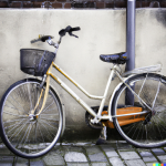 由dall - e2人工智能平台生成的图像显示，一辆略带扭曲的黄白色自行车，有一个篮子、后机架和橙色链护，靠在灰色立管附近的白色灰泥底座的砖砌建筑上。